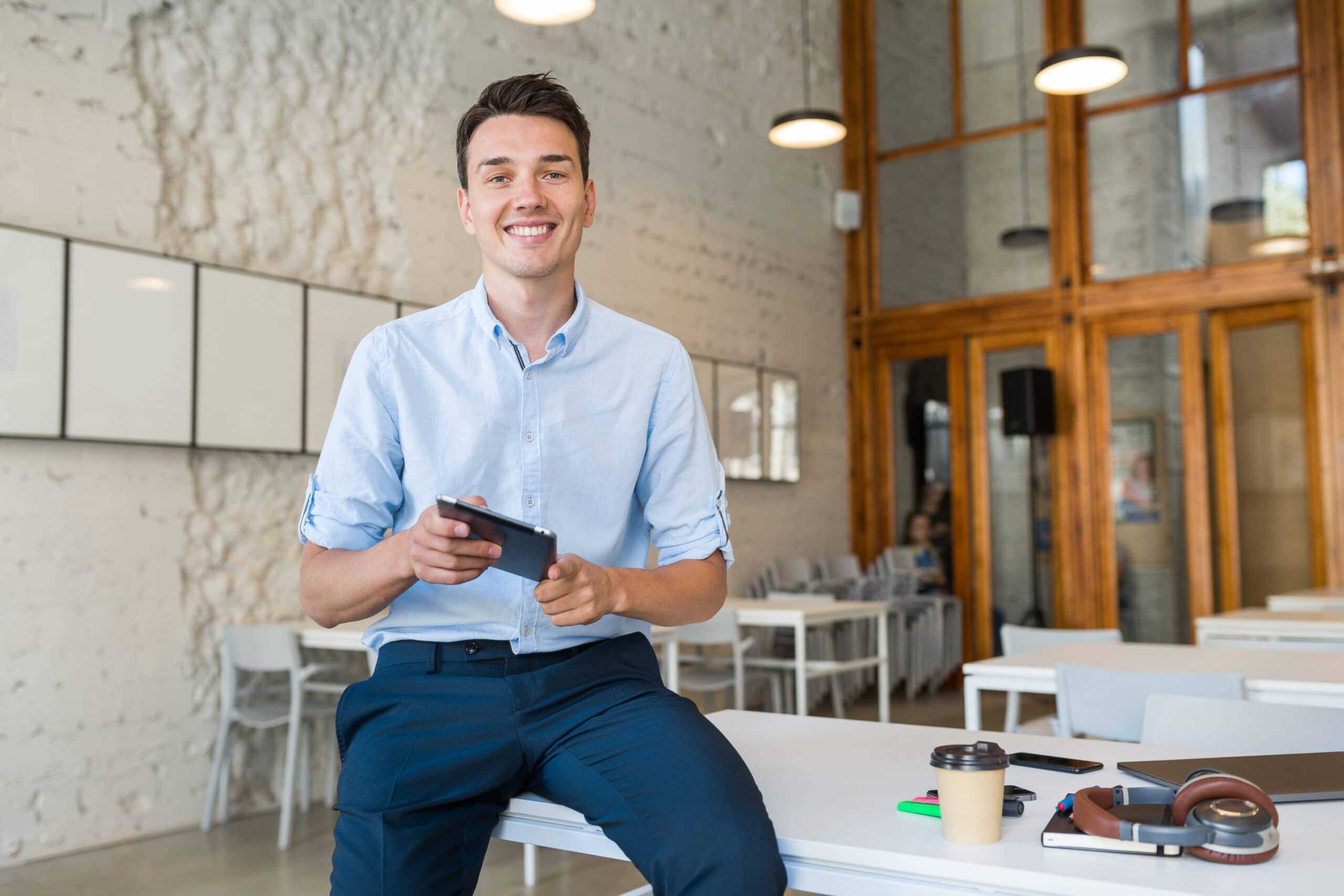 young stylish smiling man in co-working office, startup freelancer holding using tablet, modern office room workplace, student education online